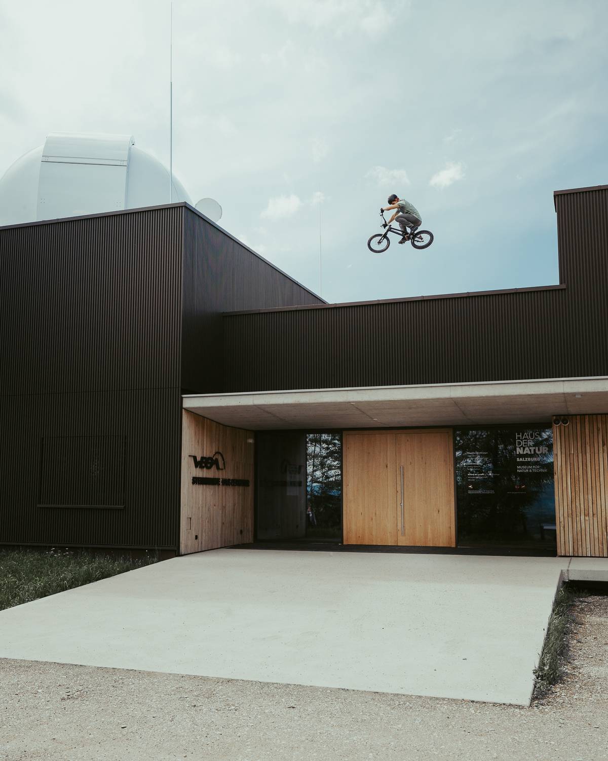 Rider on a bike in mid-air above the roof of a dark building with a dome