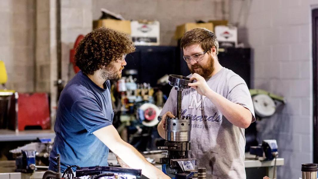 Two students operating machining equipment while assembling a mechanical component in a workshop