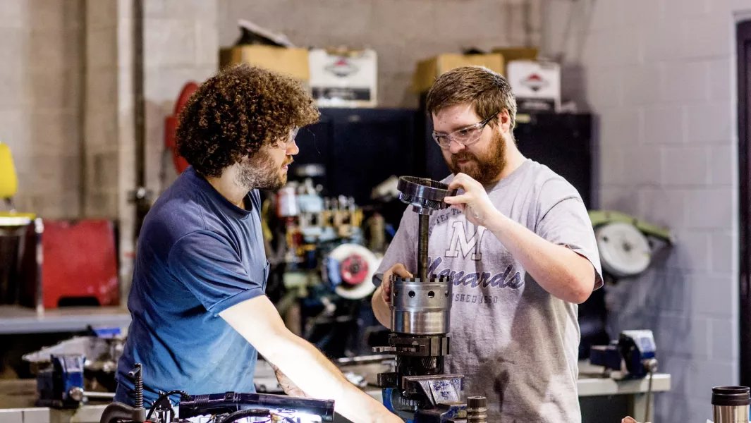 Two students operating machining equipment while assembling a mechanical component in a workshop