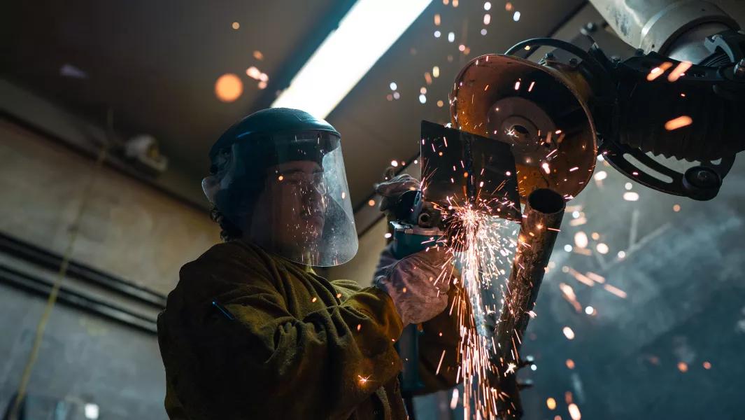 Worker using a grinder on a metal piece as sparks scatter around
