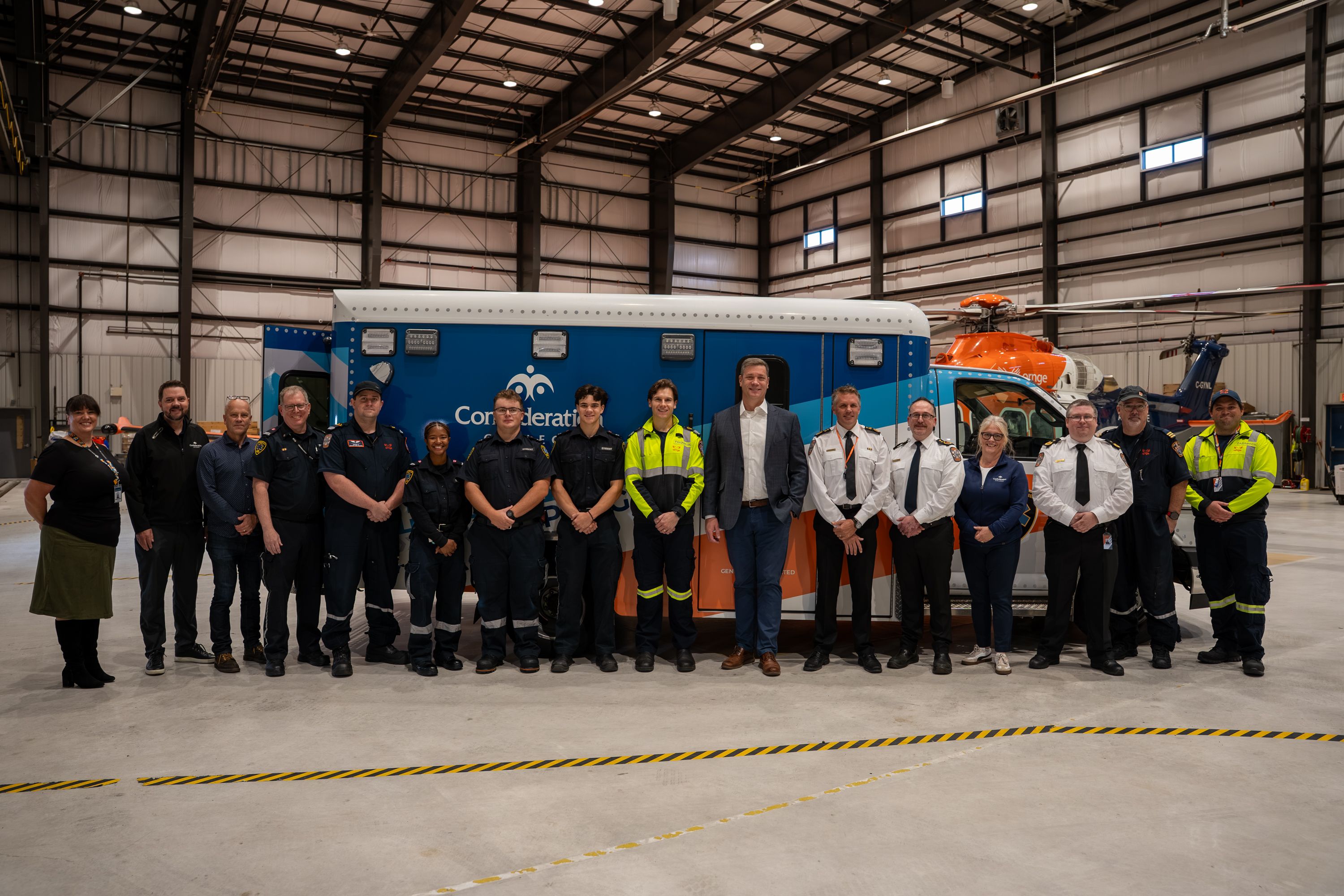 Group of people standing in front of a blue and orange ambulance inside a hangar