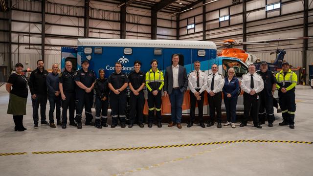 Group of people standing in front of a blue and orange ambulance inside a hangar