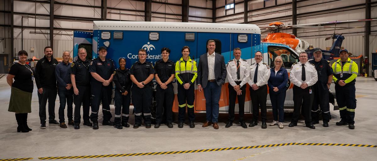 Group of people standing in front of a blue and orange ambulance inside a hangar