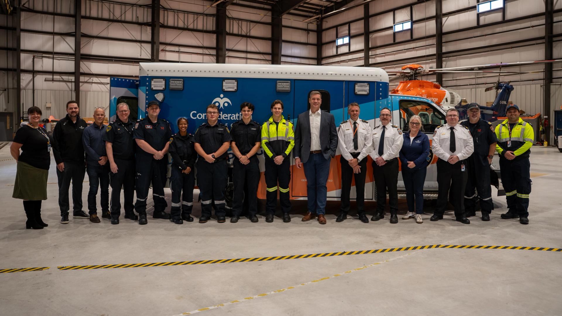 Group of people standing in front of a blue and orange ambulance inside a hangar