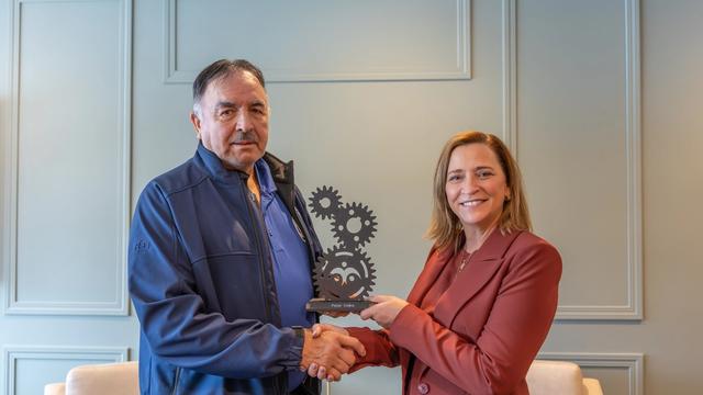 Peter Collins receives a gear-shaped award while shaking hands with a presenter