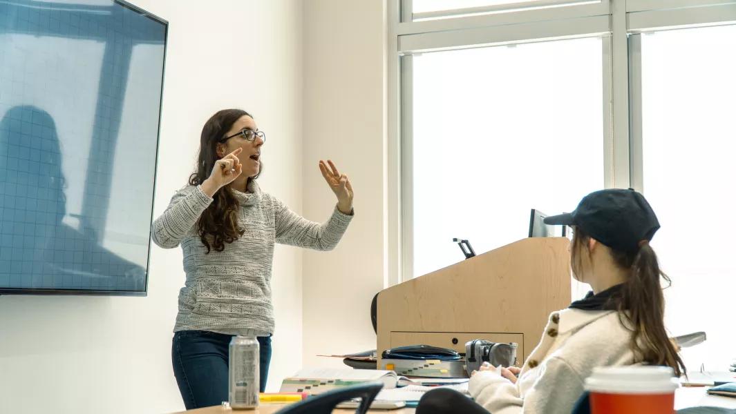 Instructor teaching in a classroom while a student listens