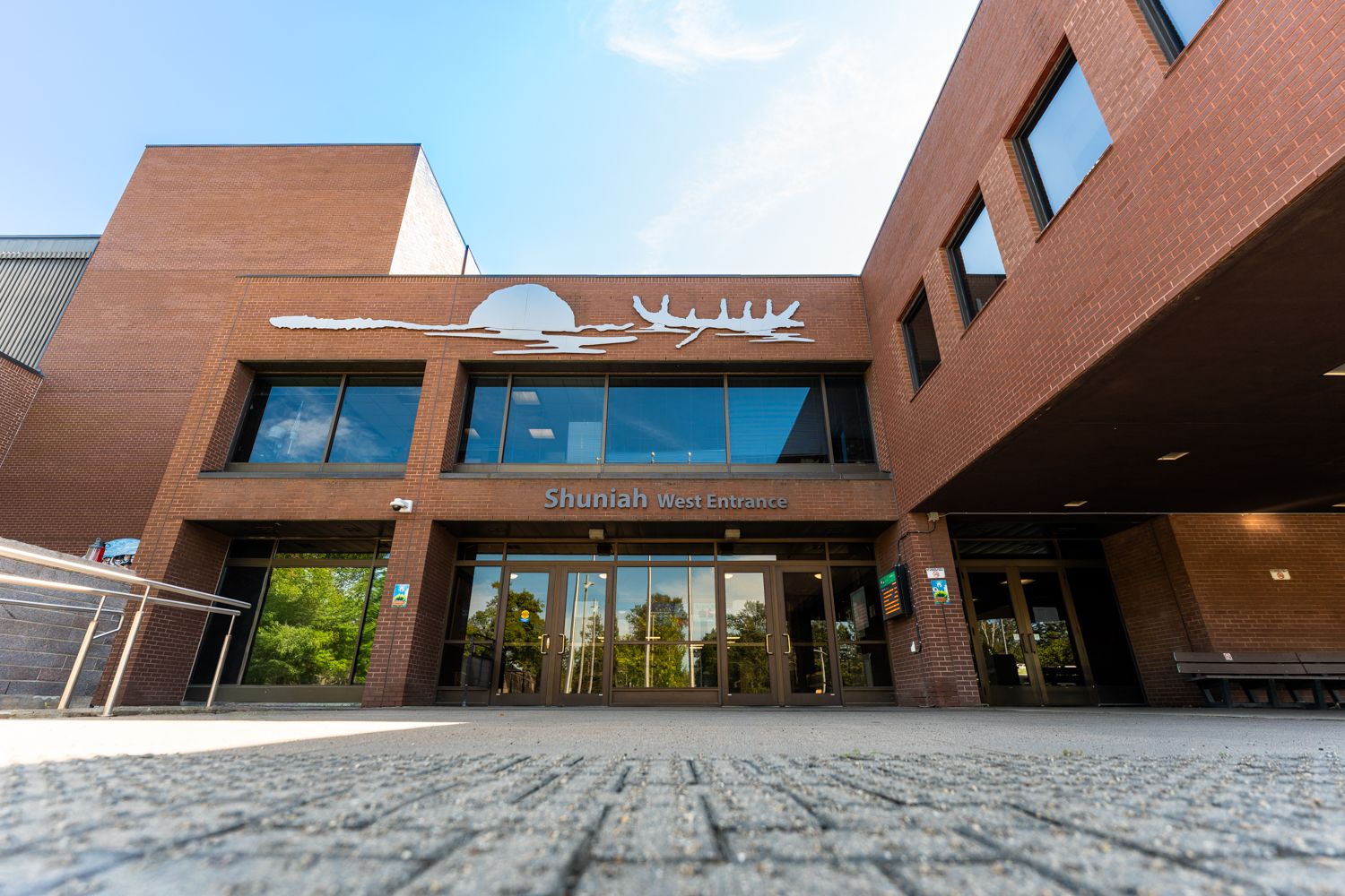 Brick campus entrance with glass doors and the sign “Shuniah West Entrance”