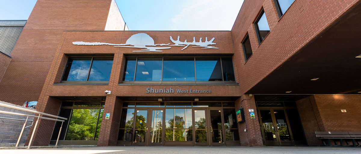 Brick entrance marked “Shuniah West Entrance,” with glass doors, upper windows and a metal silhouette above.