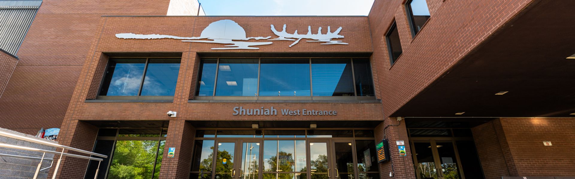 Brick campus entrance with glass doors and the sign “Shuniah West Entrance”