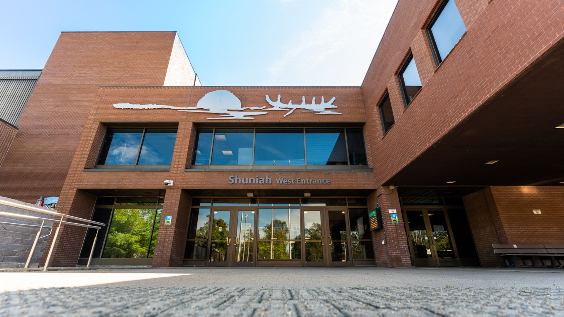 Brick entrance marked “Shuniah West Entrance,” with glass doors, upper windows and a metal silhouette above.