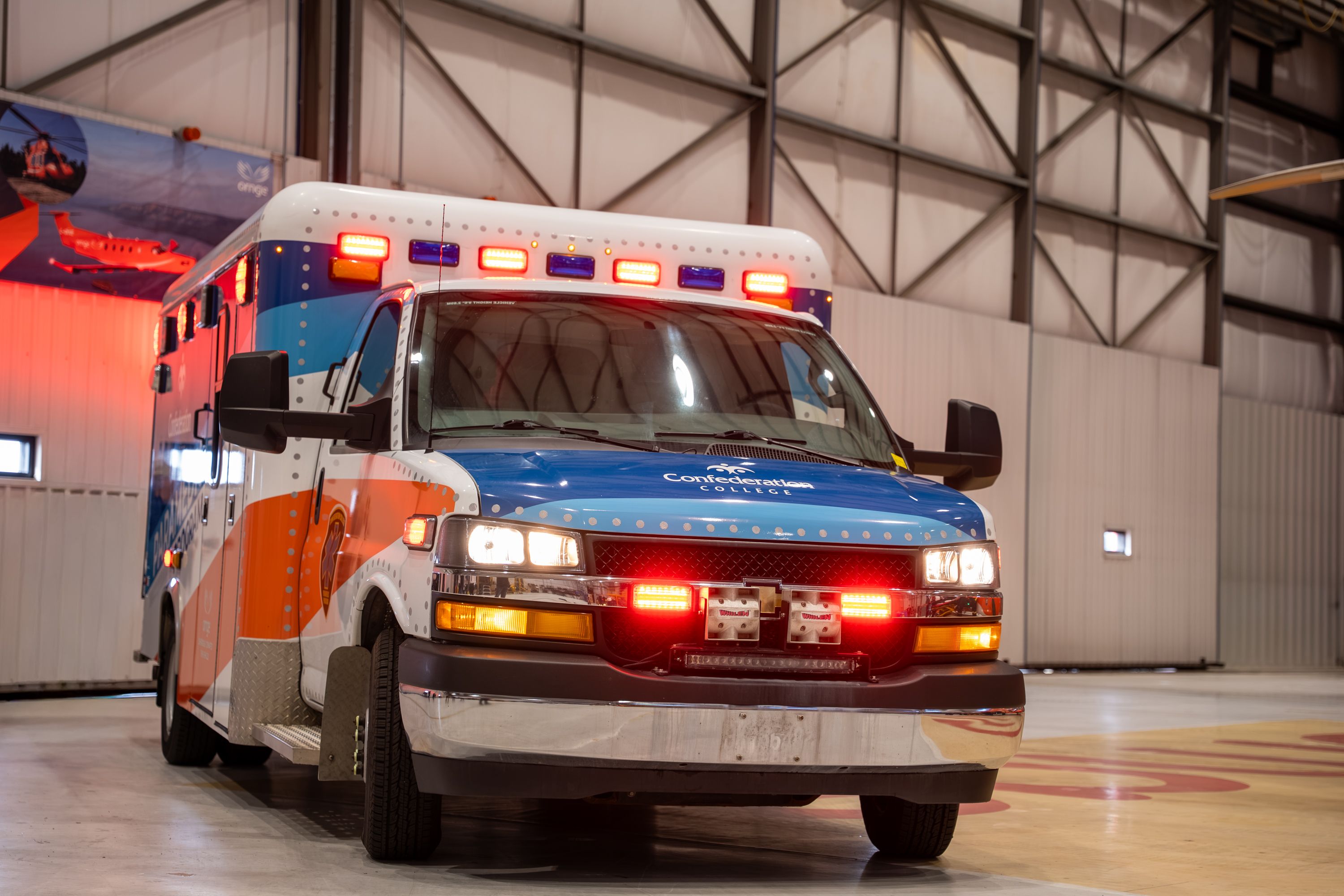 Ambulance with flashing lights parked inside a large garage-like hangar