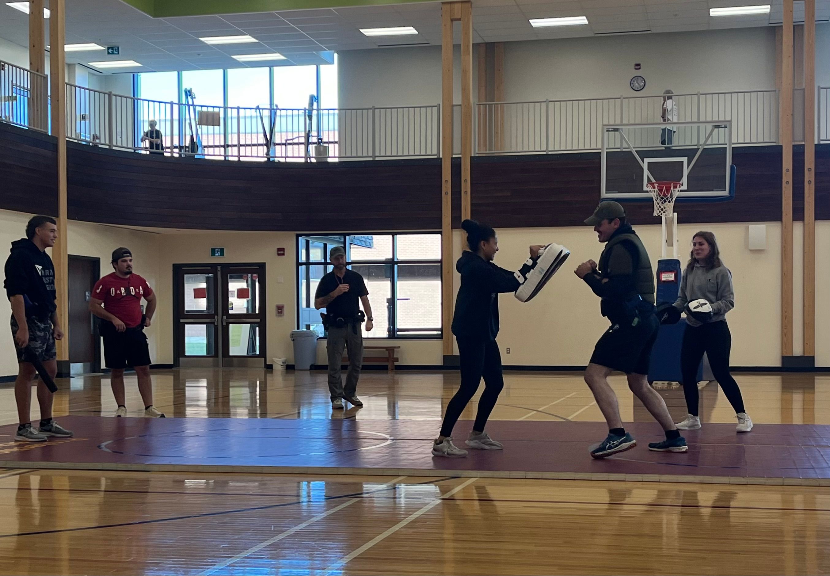 Students practice defensive tactics with pads in a gymnasium