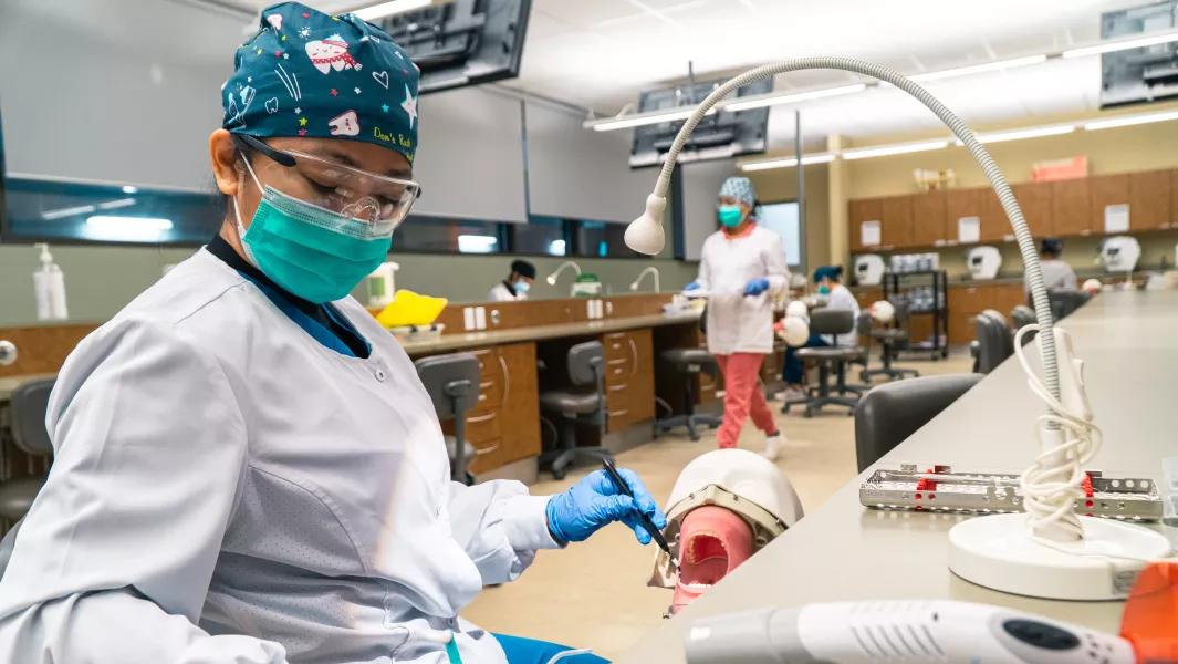 Dental assisting student performing a procedure on a dental mannequin in the lab