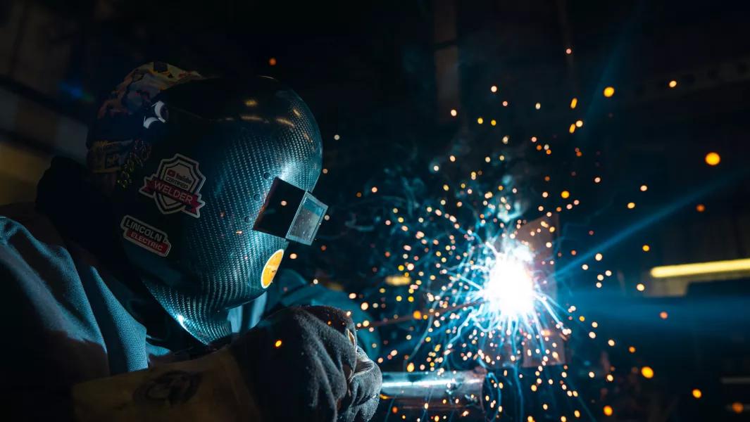 Welder in a dark workshop creating bright sparks while working on metal