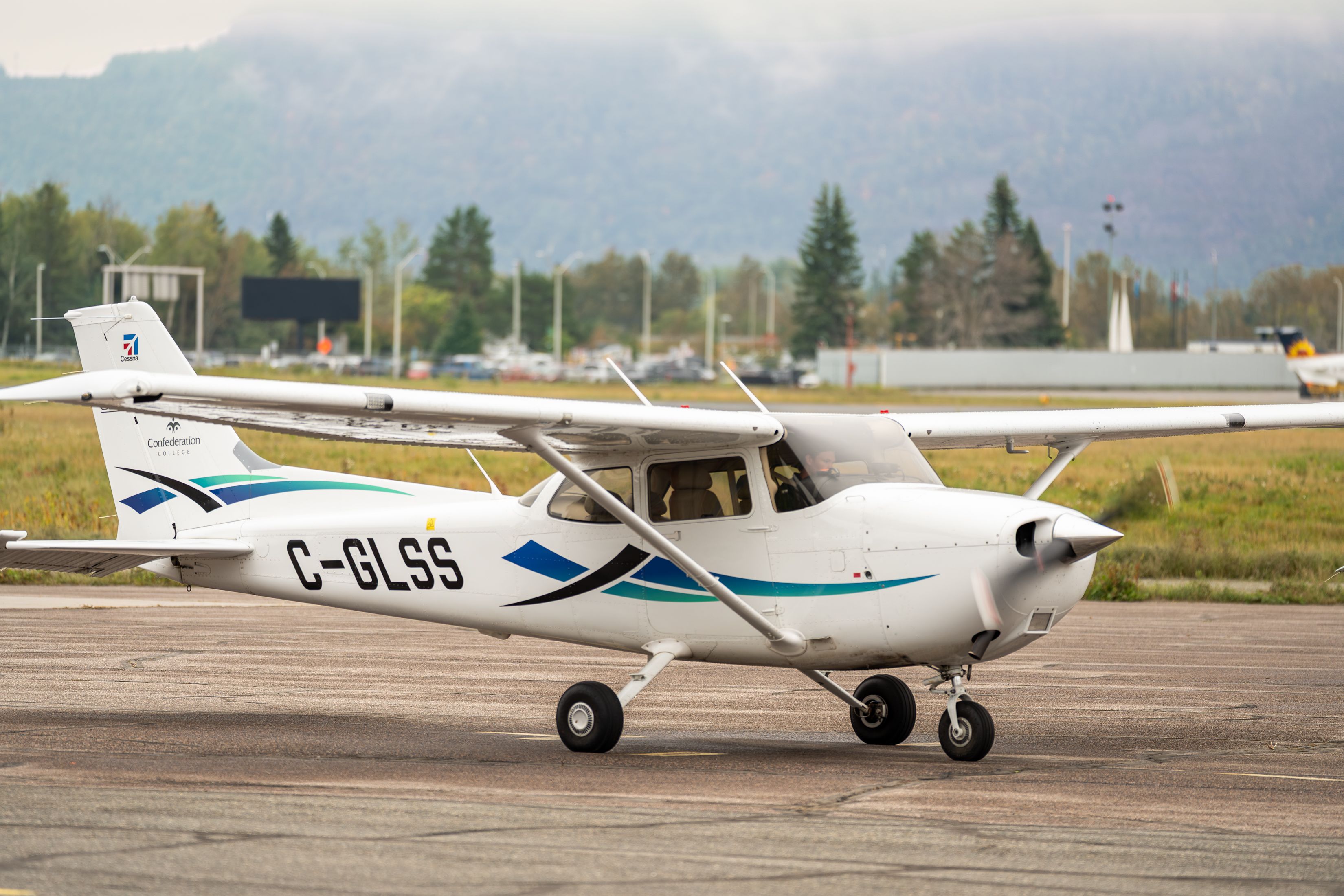 A white Confederation College single-engine plane with registration C-GLSS sits on an airport runway.