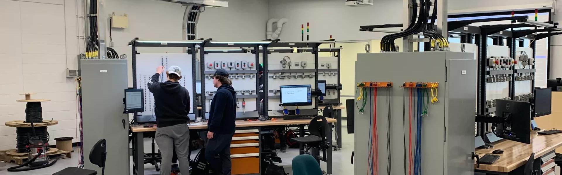 Students working on electrical control systems in a modern automation lab with computers and wiring equipment