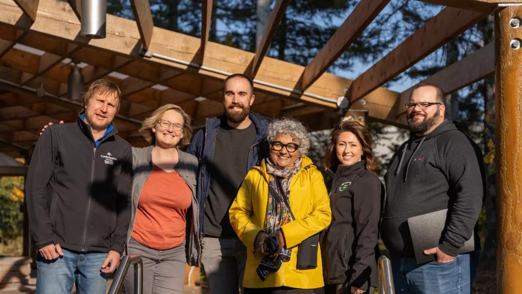 Group of staff standing together under a wooden pavilion on campus