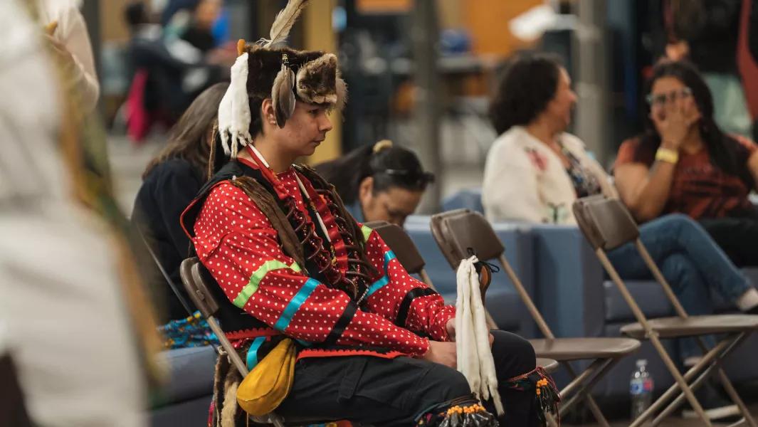 Person in vibrant regalia seated and observing a community gathering