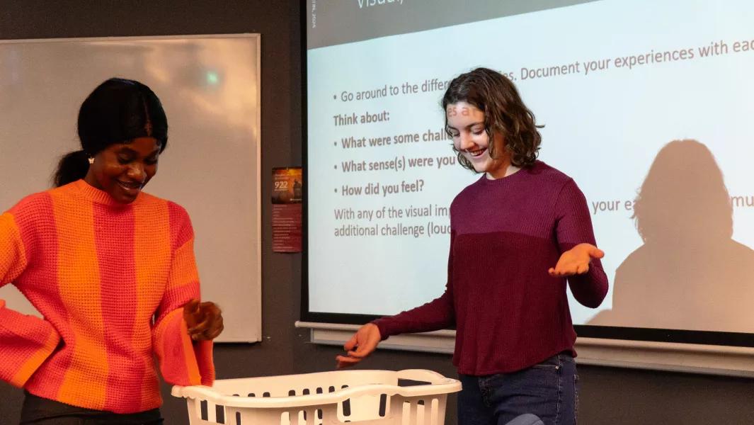 Two students leading a hands-on demonstration in front of a projected slide