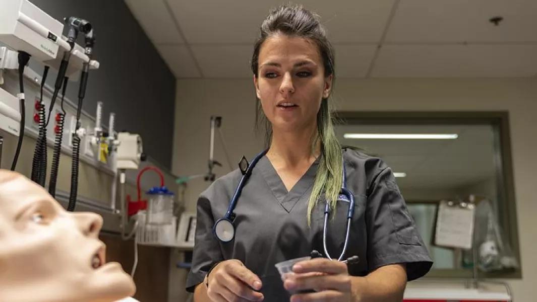 Nursing student preparing medication beside a patient mannequin