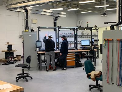 Students working at computer stations in an electrical engineering lab with control panels and wiring