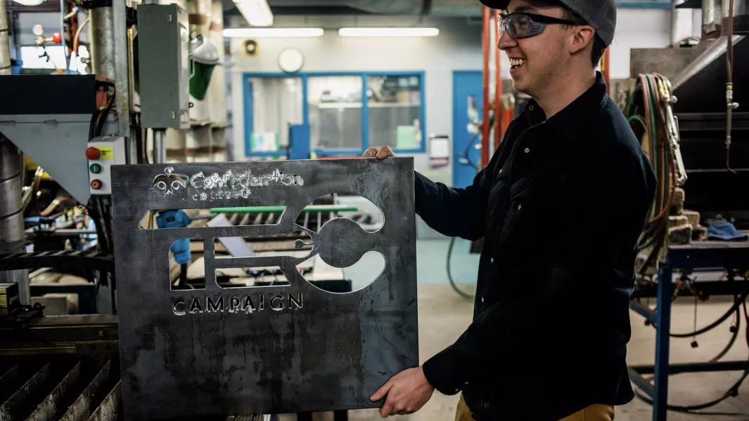 Student holding a cut metal sign featuring a program logo