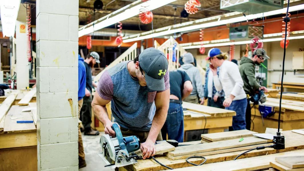 Carpentry student cutting wood with a circular saw while classmates work nearby