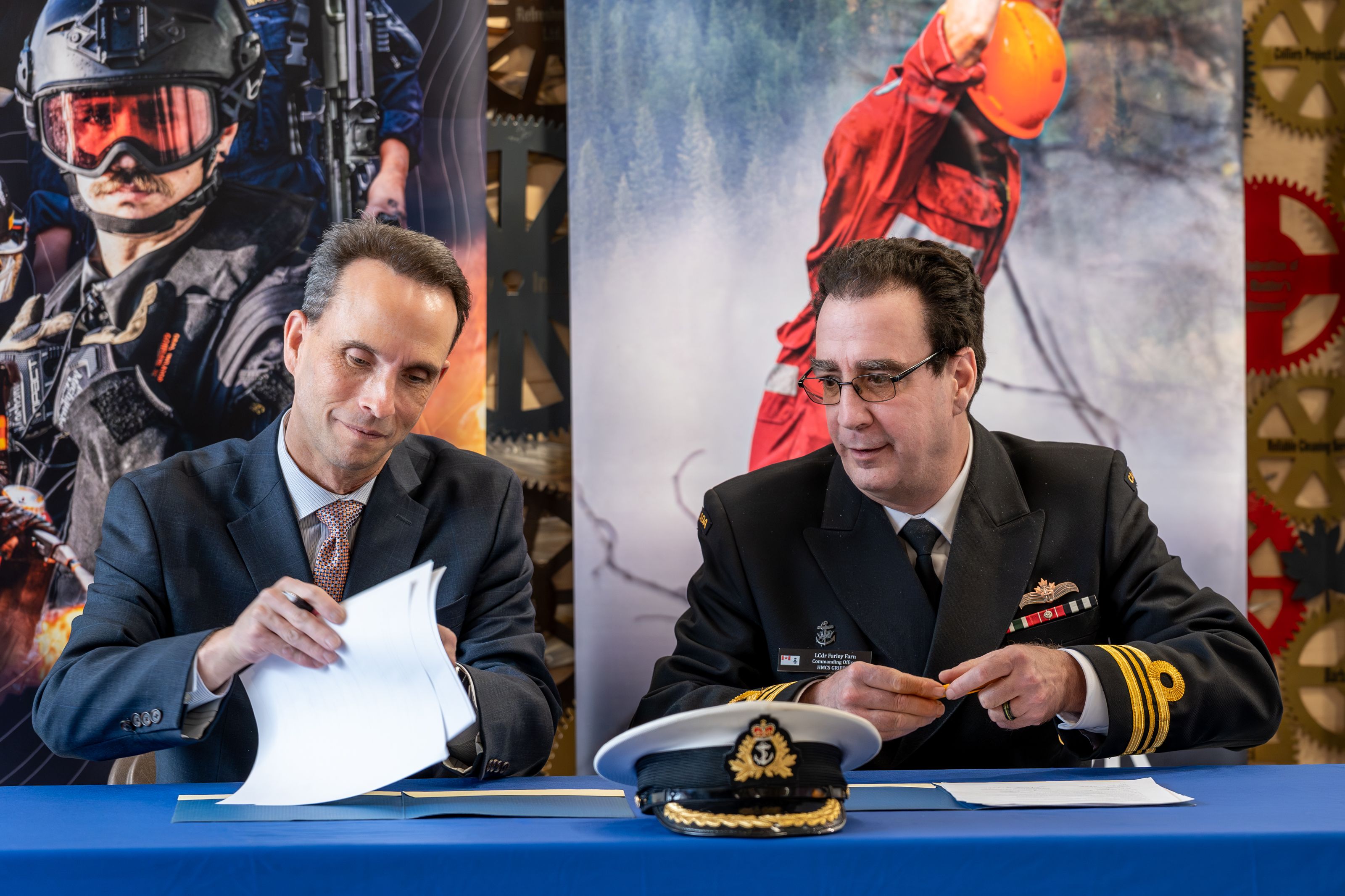 Two officials sign documents at a table during a Royal Canadian Navy partnership event at Confederation College