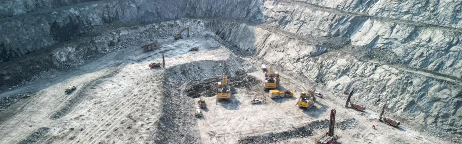 Aerial view of an open-pit mine with heavy machinery working on terraced rock walls and gravel ground