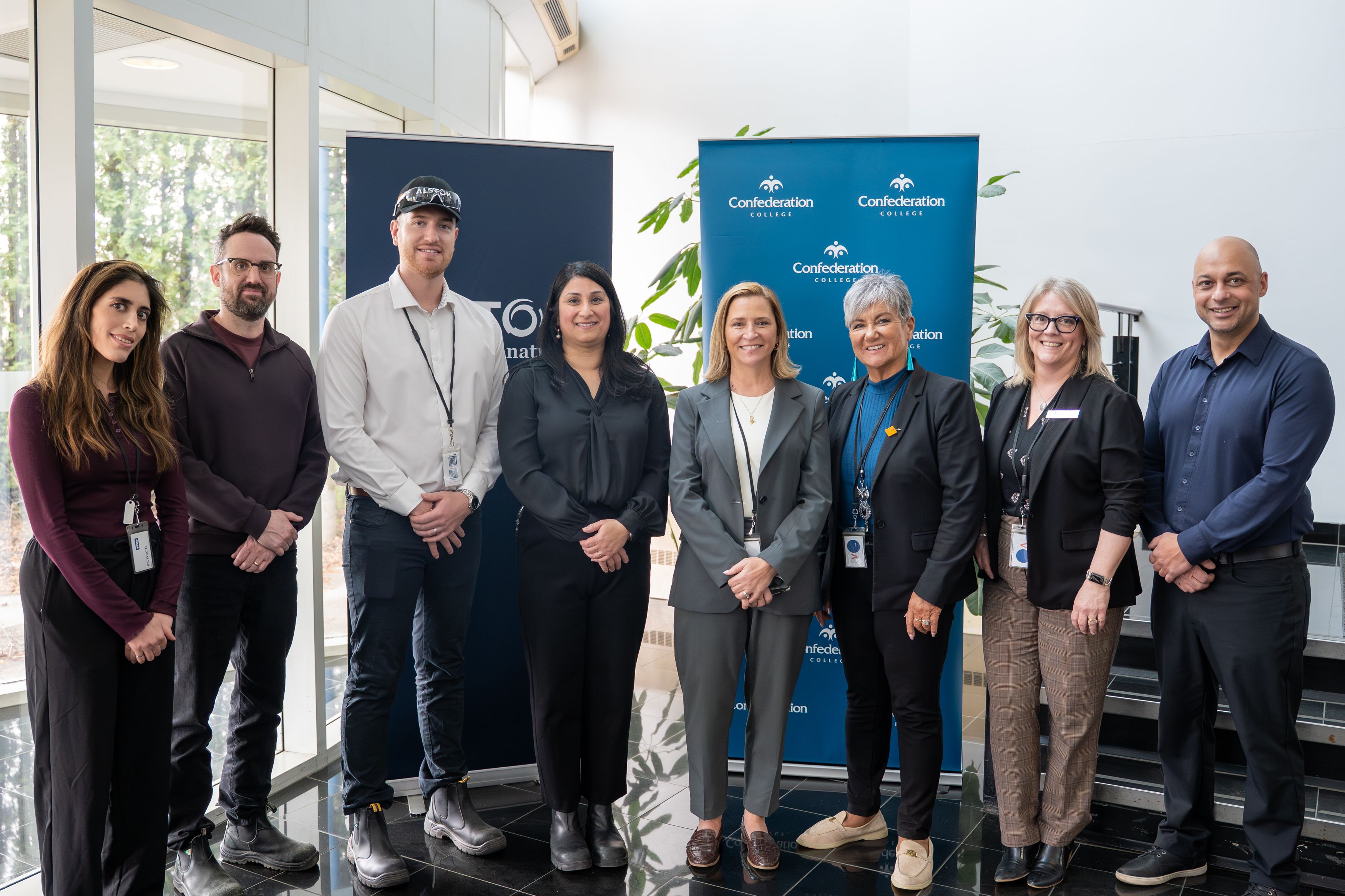 Group of persons posing indoors in front of Confederation College and Alstom banners during partnership announcement