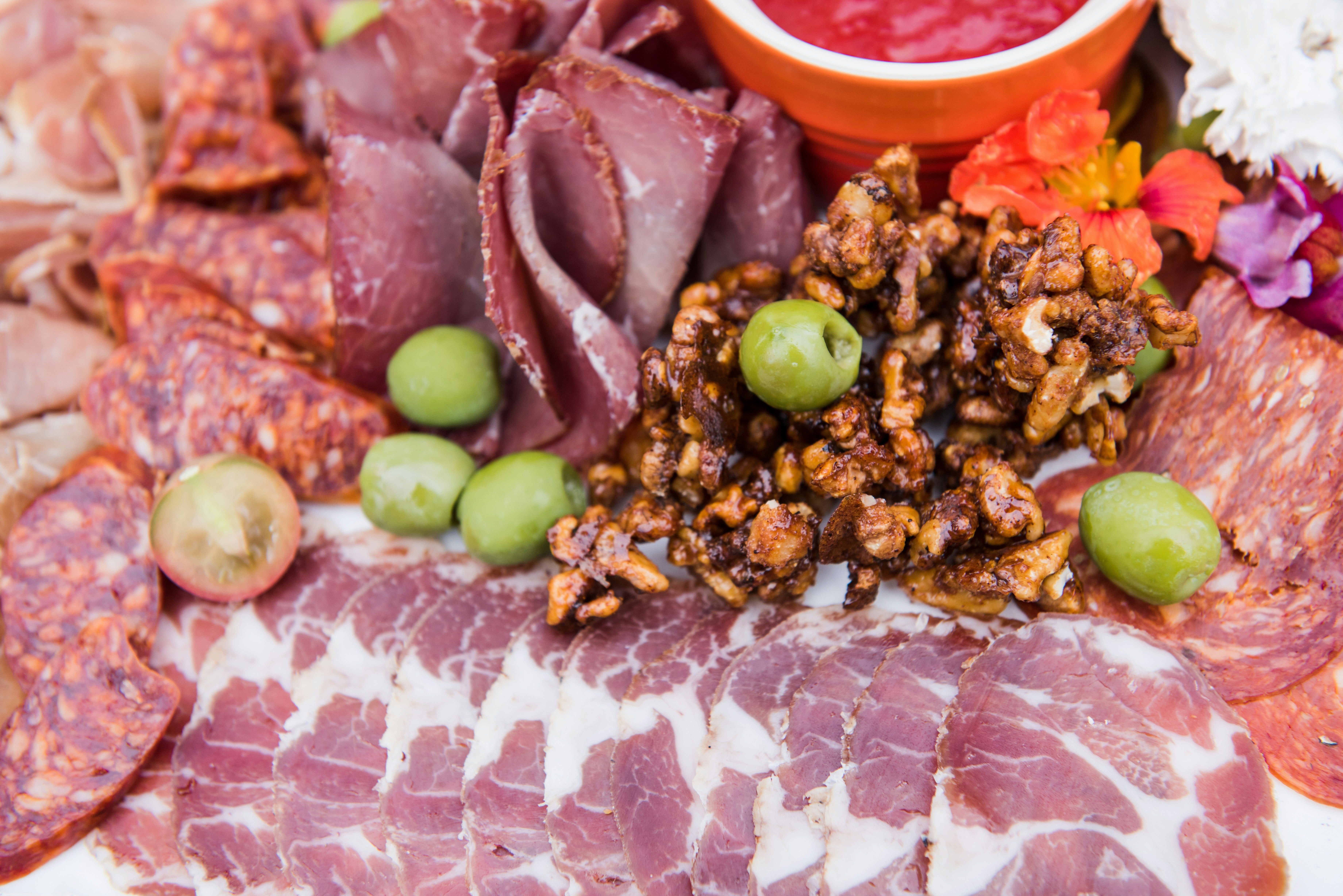 Assorted cured meats with green olives, walnuts, and a small bowl of red sauce on a platter