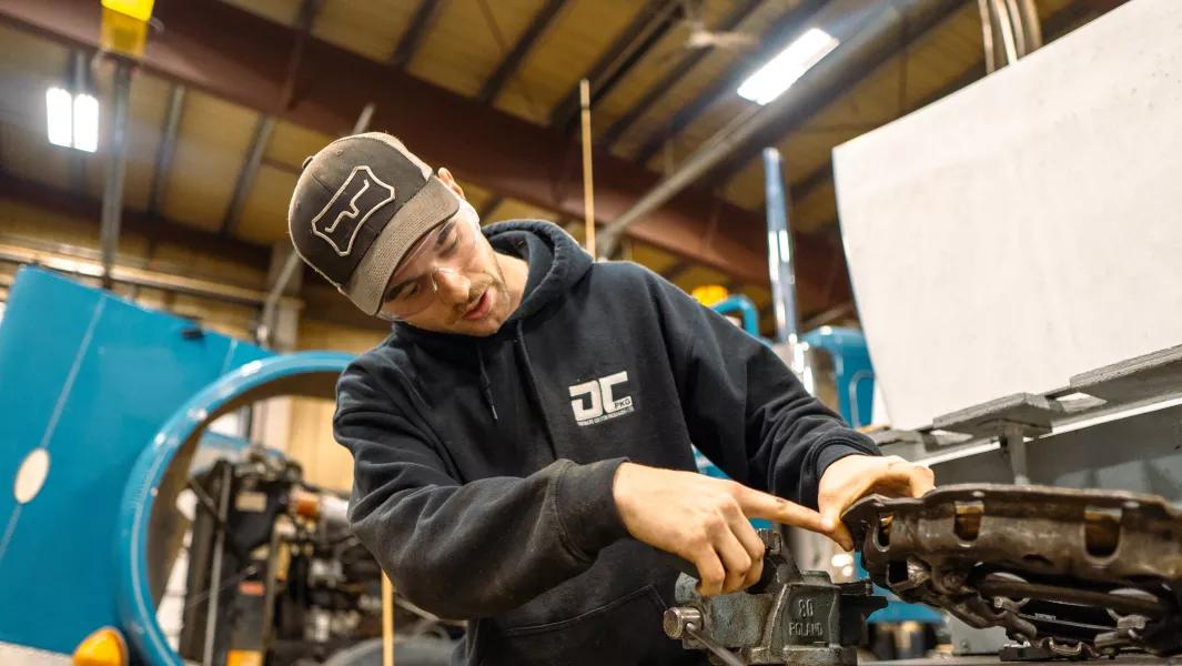 Student examining and pointing at a mechanical part on a workbench