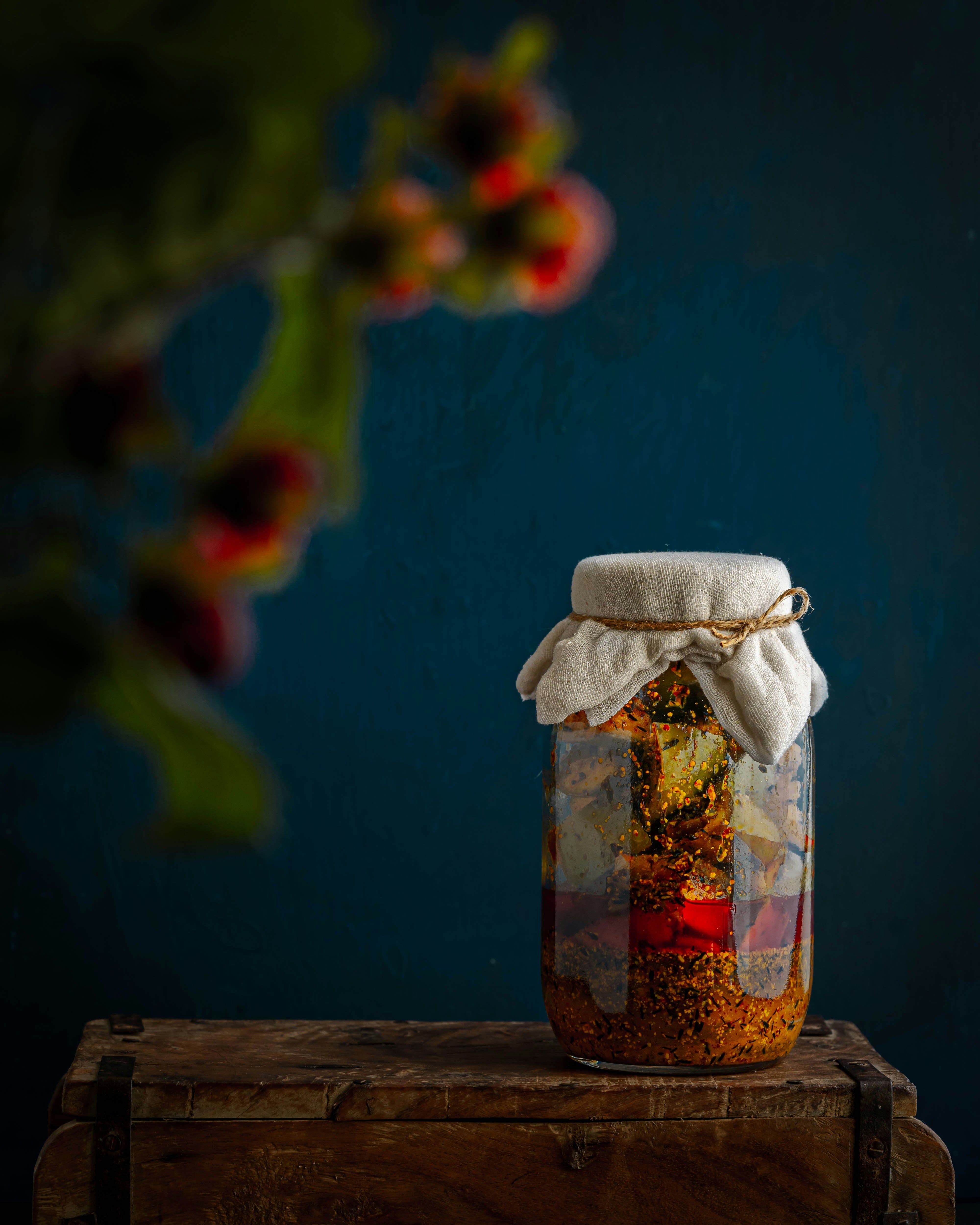 A glass jar of pickled vegetables topped with a cloth cover, sitting on a wooden crate.