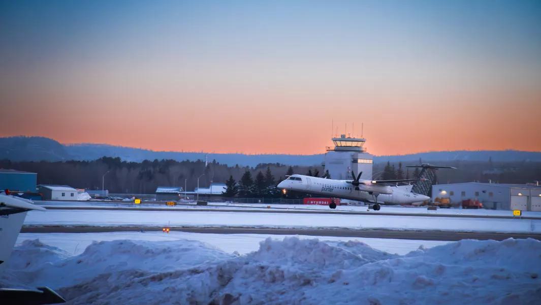 Airliner taxiing on a snowy runway at sunset near the control tower