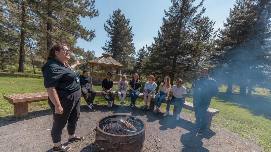 Outdoor group gathered around a fire pit listening to a facilitator