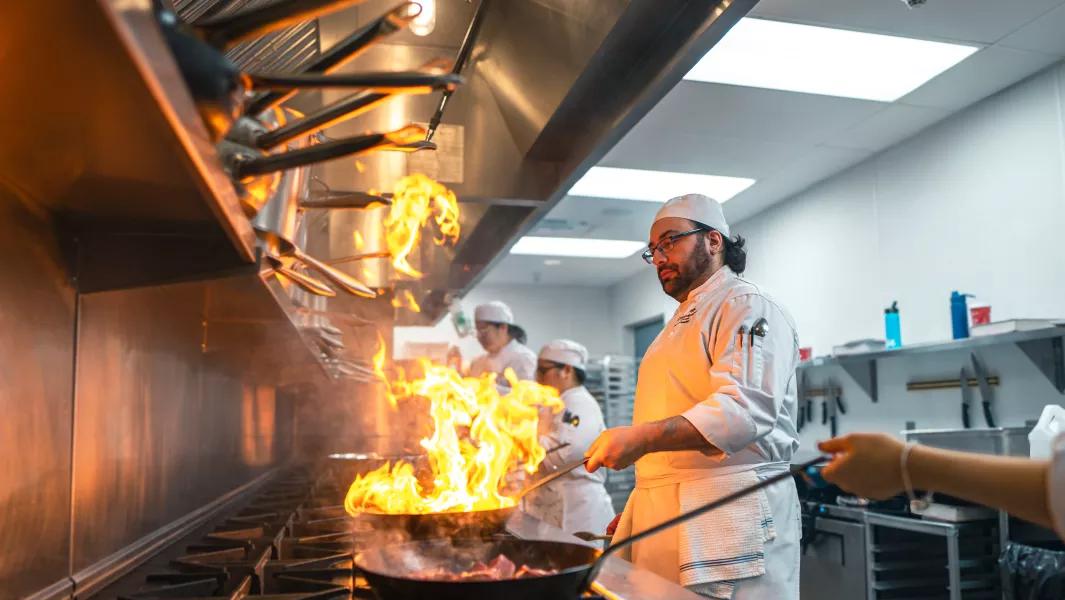 Culinary student cooking over open flames on a commercial stove during class