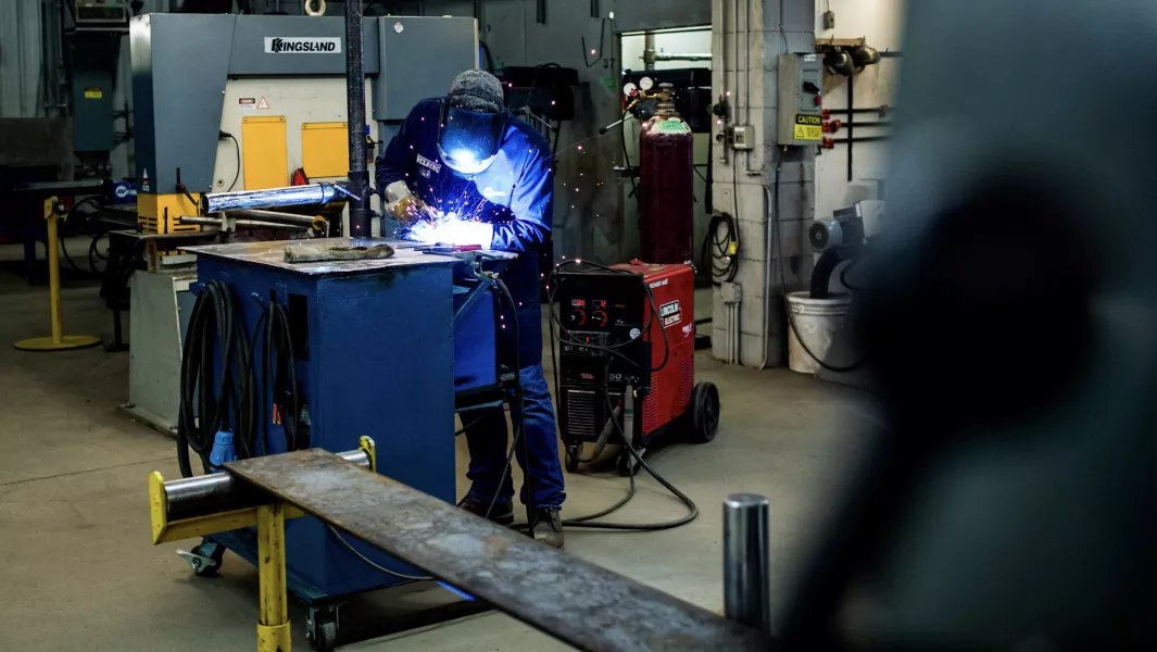 Student welding metal components at a workstation in an industrial training shop
