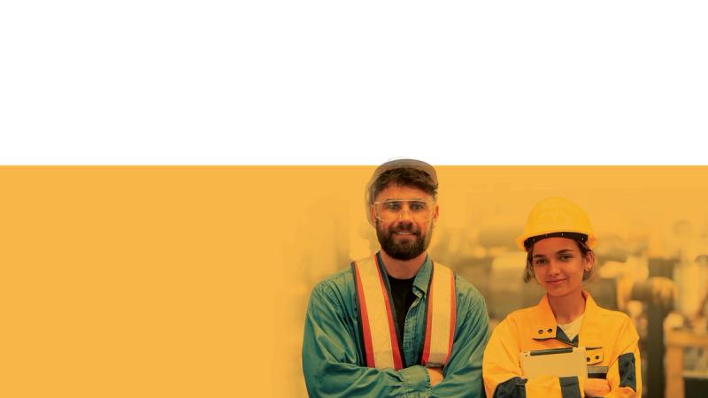 Two construction workers wearing safety vests and hard hat standing together at an industrial site