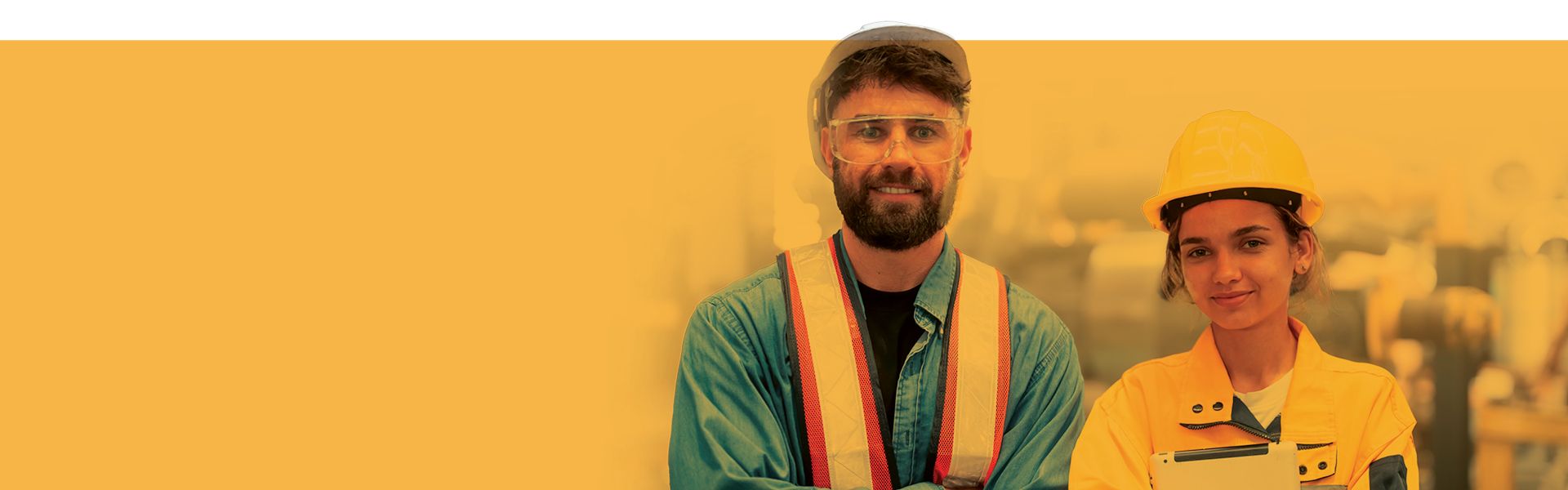 Two construction workers wearing safety vests and hard hat standing together at an industrial site