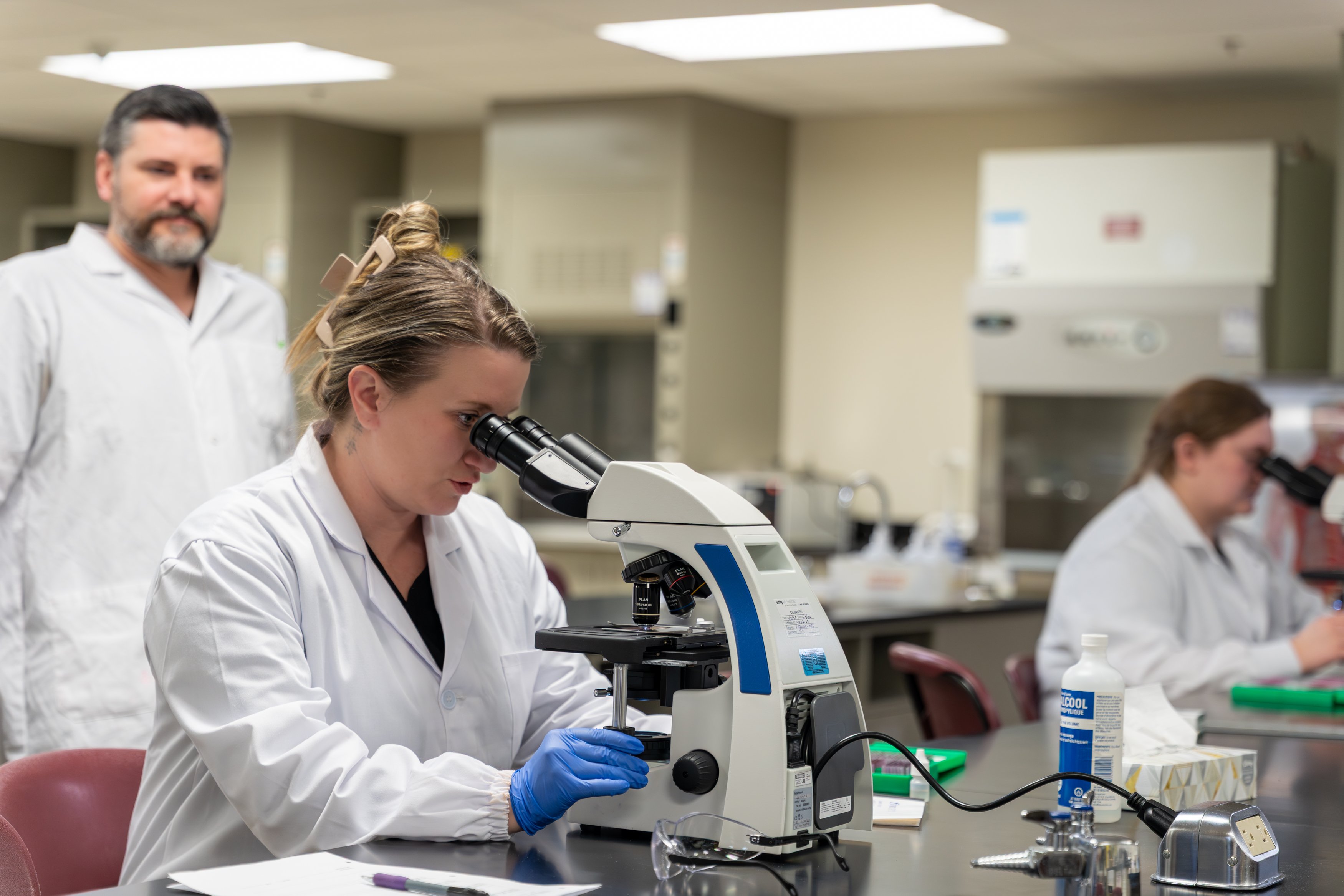 Students in lab coats examining samples with microscopes in a science laboratory