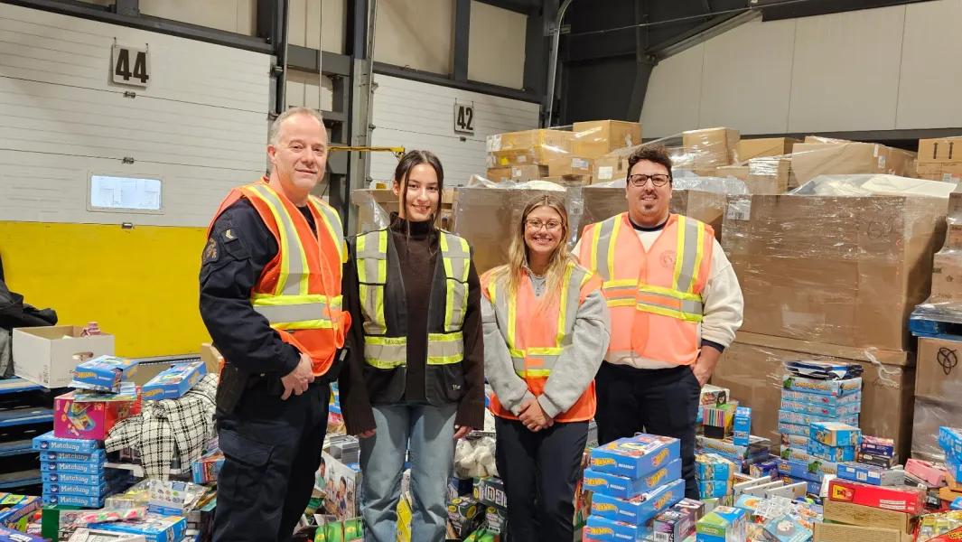 Volunteers in safety vests stand among donated toys and supplies in a warehouse