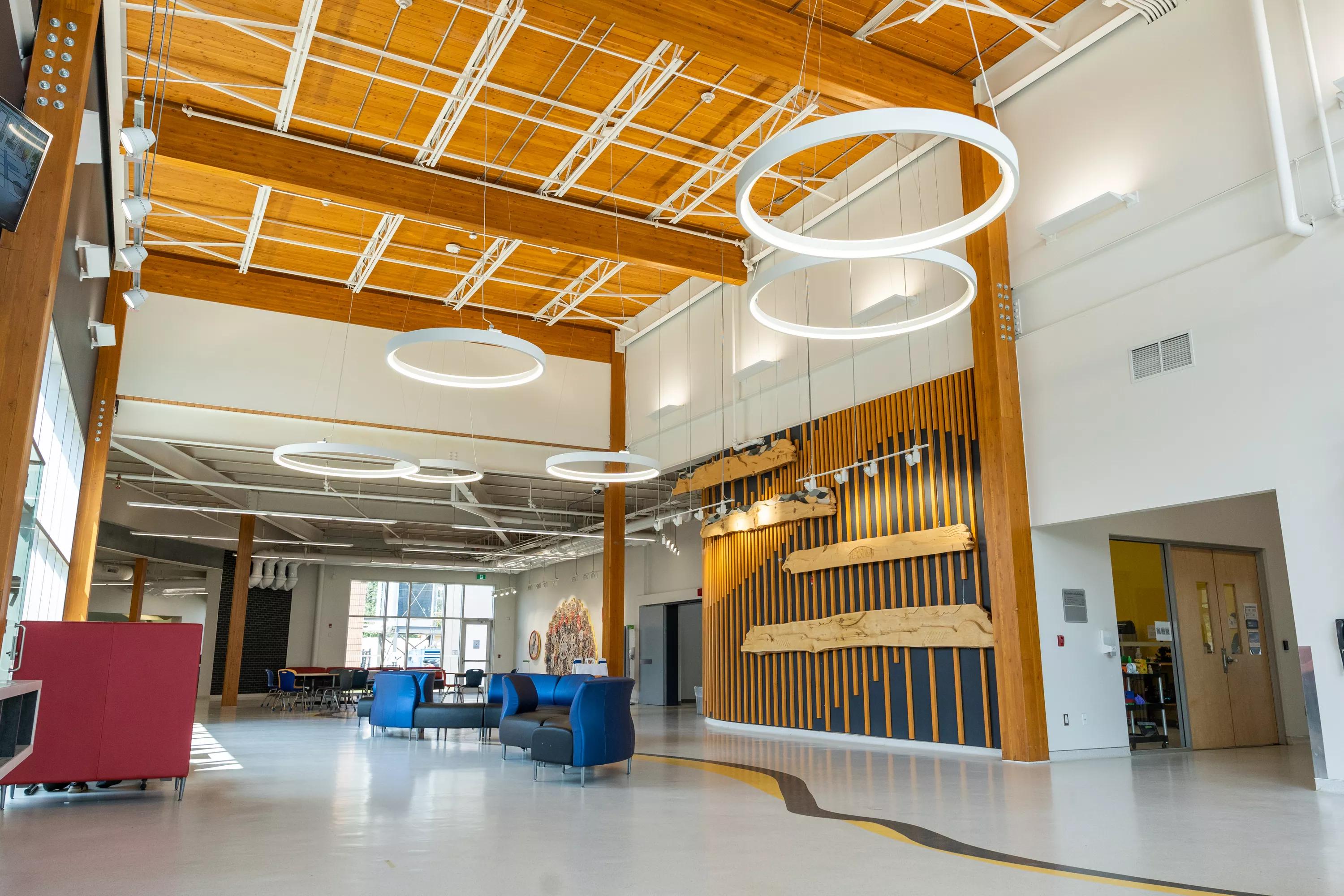 Bright, open campus atrium with wood beams, circular lights, and seating areas
