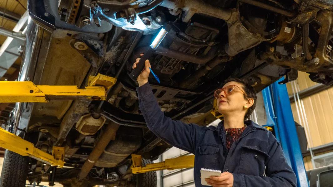 Instructor inspecting the underside of a lifted vehicle while taking notes