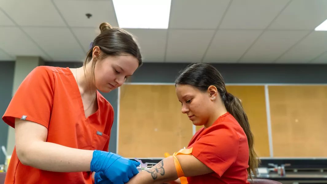Student practicing a medical blood-draw procedure on a class partner