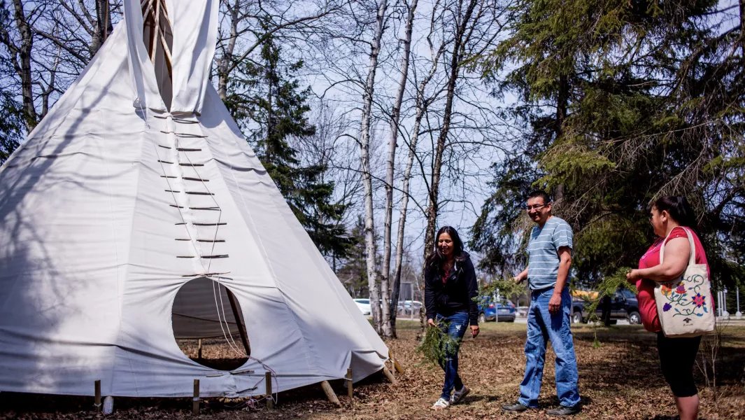People standing outside a large white tipi surrounded by trees
