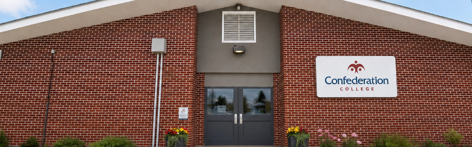 Greenstone Campus Front entrance of a red brick Confederation College building with a concrete walkway and flower planters
