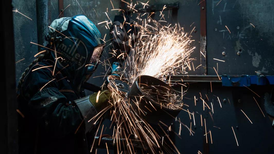 Welder shaping a metal pipe with intense sparks in a fabrication booth