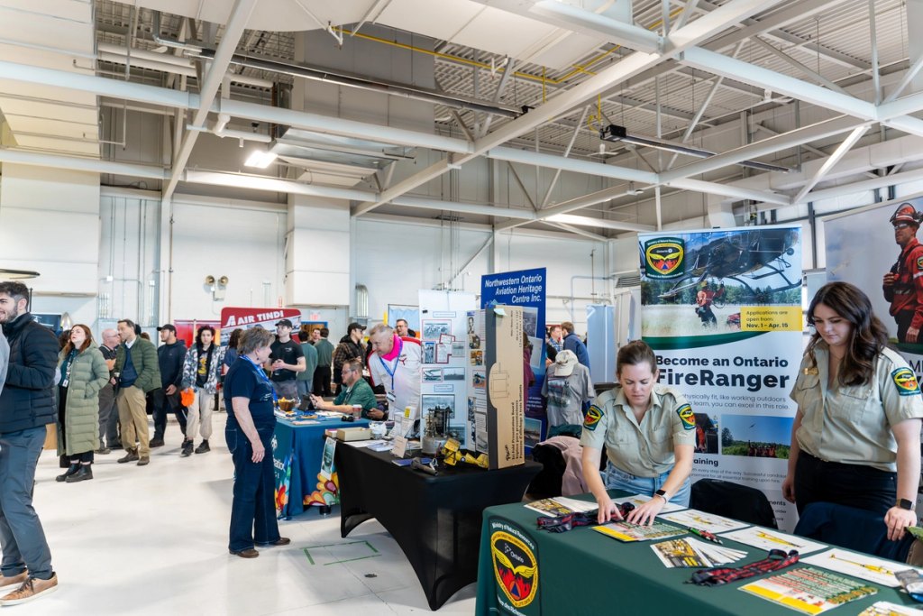 Crowd of students and employers networking at Aviation Day booths inside Confederation College aviation hangar