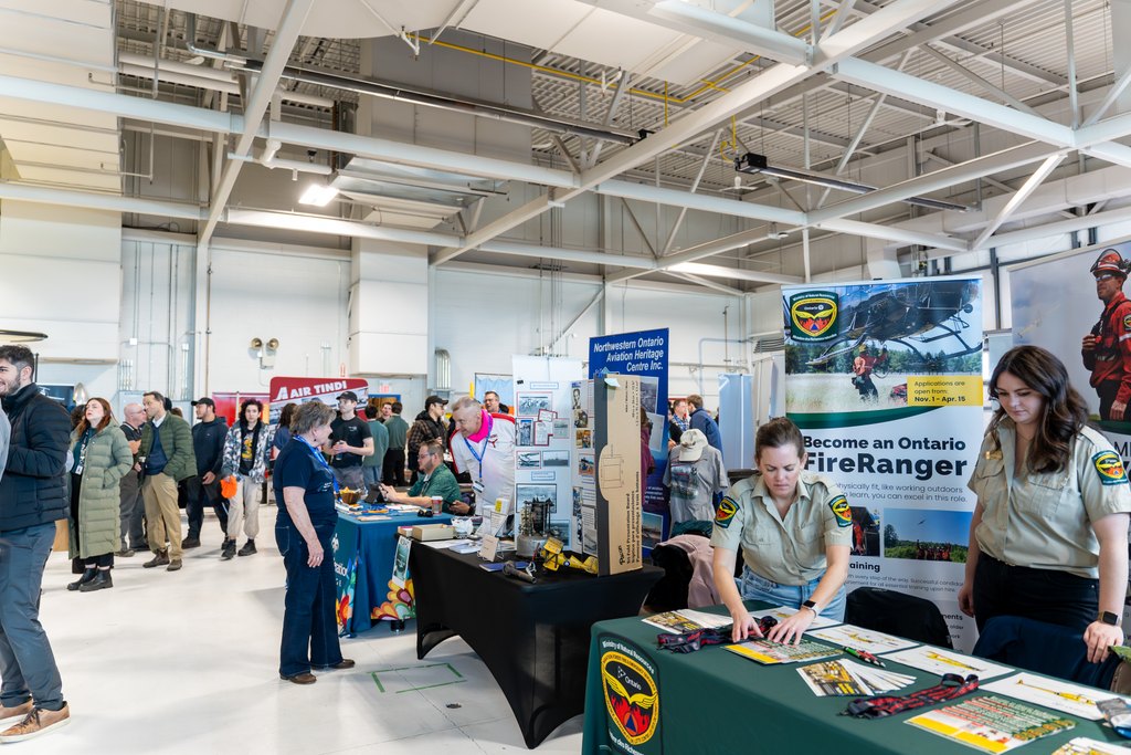 Crowd of students and employers networking at Aviation Day booths inside Confederation College aviation hangar