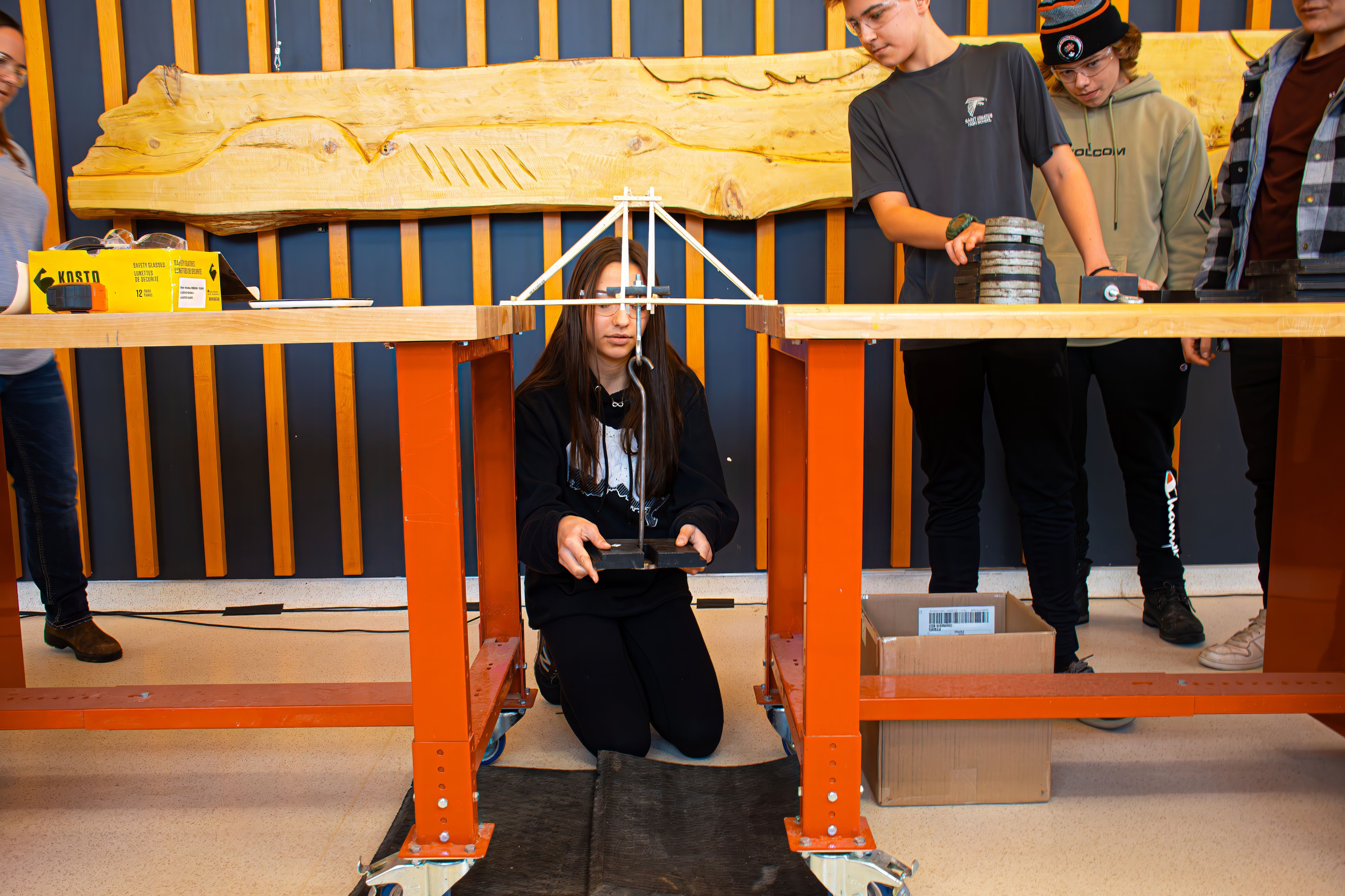 Students testing a model bridge with weights during a Confederation College engineering challenge